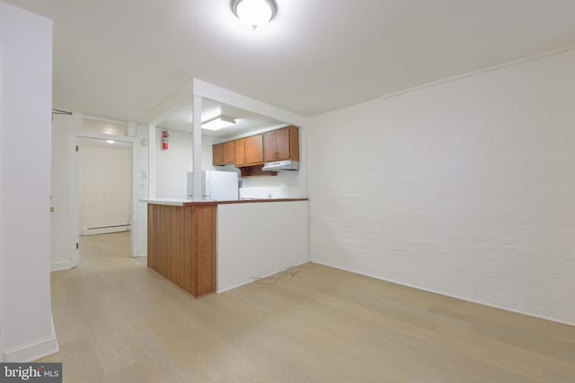 kitchen with under cabinet range hood, freestanding refrigerator, light wood-type flooring, brown cabinetry, and brick wall