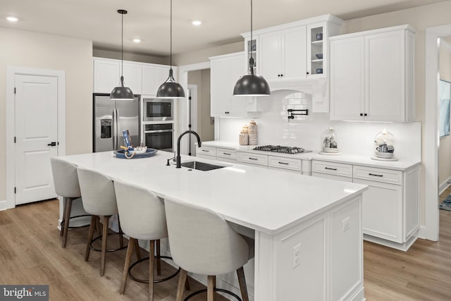 kitchen featuring stainless steel appliances, an island with sink, sink, white cabinetry, and backsplash