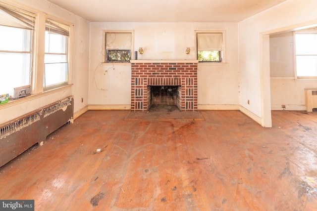 unfurnished living room featuring a brick fireplace, radiator, and a healthy amount of sunlight