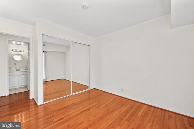 unfurnished bedroom with ensuite bath, a closet, sink, and wood-type flooring