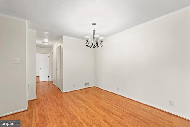 empty room featuring light wood-type flooring and a chandelier