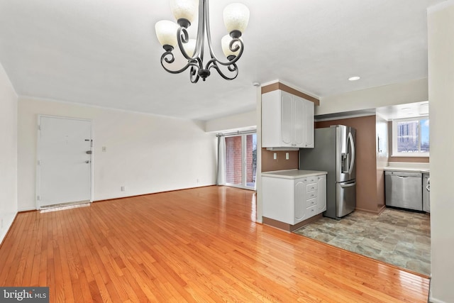 kitchen with an inviting chandelier, light hardwood / wood-style flooring, hanging light fixtures, stainless steel appliances, and white cabinets