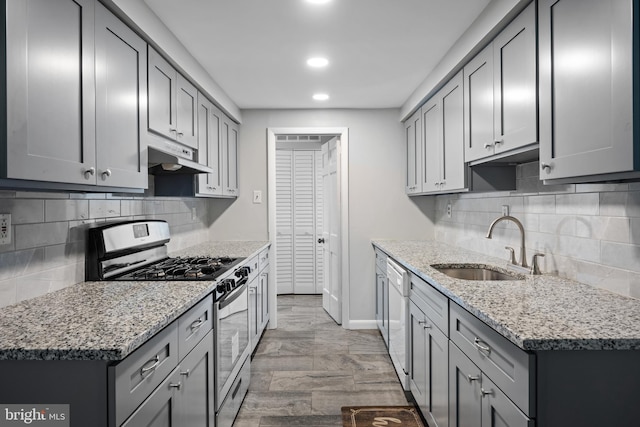 kitchen featuring gas range, light stone counters, gray cabinetry, and sink