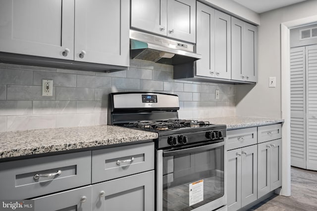 kitchen featuring light stone counters, gas range oven, light hardwood / wood-style floors, decorative backsplash, and gray cabinets