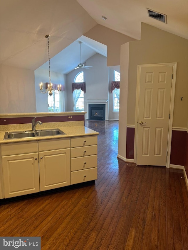 kitchen with decorative light fixtures, vaulted ceiling, sink, white cabinetry, and ceiling fan with notable chandelier