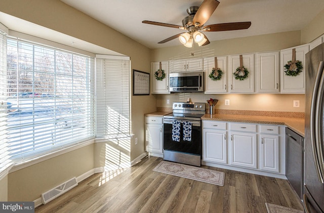 kitchen featuring ceiling fan, appliances with stainless steel finishes, hardwood / wood-style floors, and white cabinets