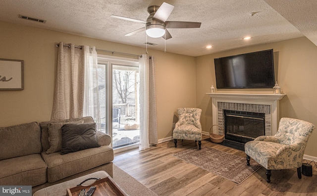 living room featuring ceiling fan, a textured ceiling, a fireplace, and light hardwood / wood-style flooring