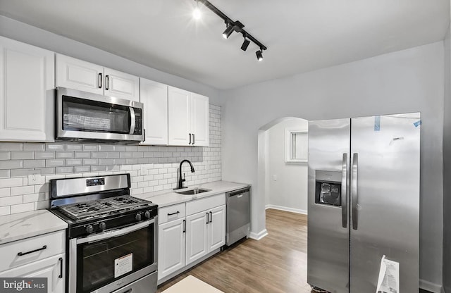 kitchen with white cabinets, stainless steel appliances, sink, light hardwood / wood-style flooring, and backsplash