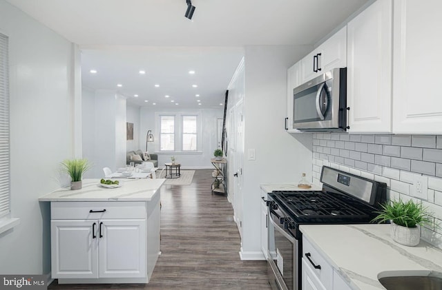 kitchen with appliances with stainless steel finishes, light stone countertops, dark wood-type flooring, decorative backsplash, and white cabinets