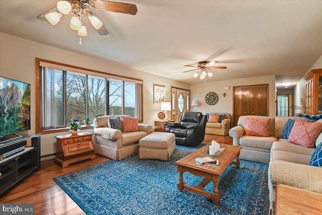 living room with wood-type flooring, baseboard heating, and ceiling fan