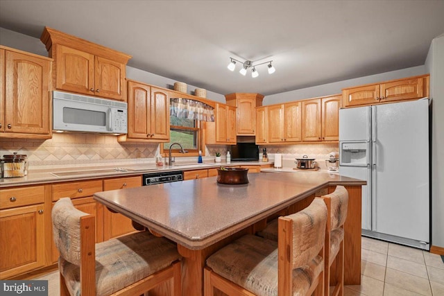 kitchen featuring white appliances, light tile patterned floors, decorative backsplash, a kitchen island, and a breakfast bar area