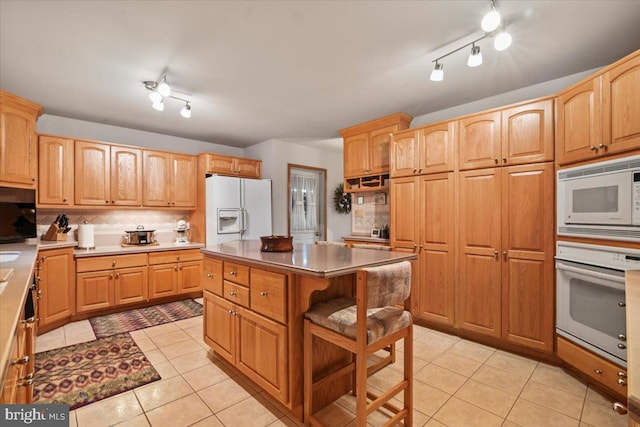 kitchen with white appliances, a kitchen breakfast bar, a center island, light tile patterned floors, and decorative backsplash