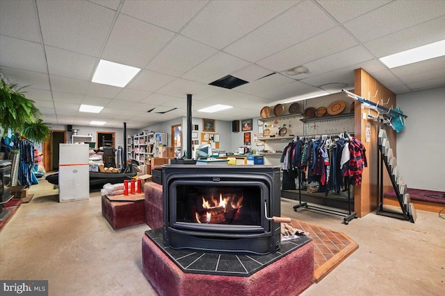 interior space featuring concrete flooring, a paneled ceiling, and a wood stove