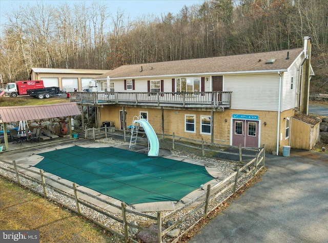 back of property featuring a garage, a balcony, a covered pool, and an outdoor structure