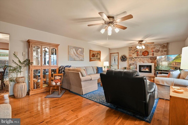 living room with hardwood / wood-style floors, ceiling fan, and a stone fireplace