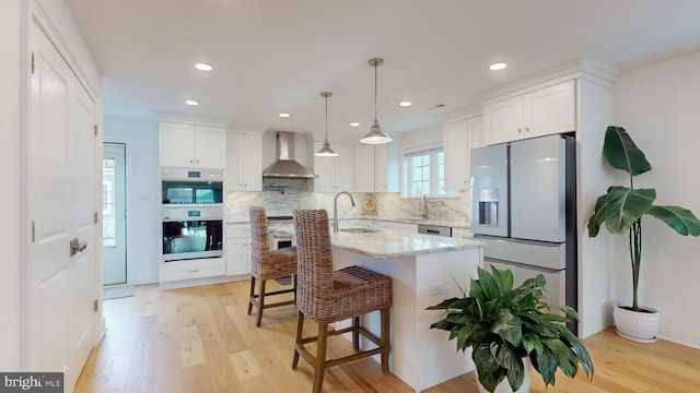 kitchen with stainless steel appliances, wall chimney range hood, and white cabinets