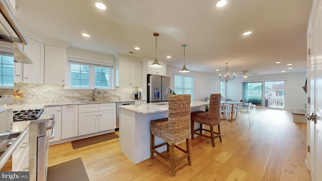 kitchen with hanging light fixtures, light hardwood / wood-style floors, a kitchen island, white cabinetry, and appliances with stainless steel finishes