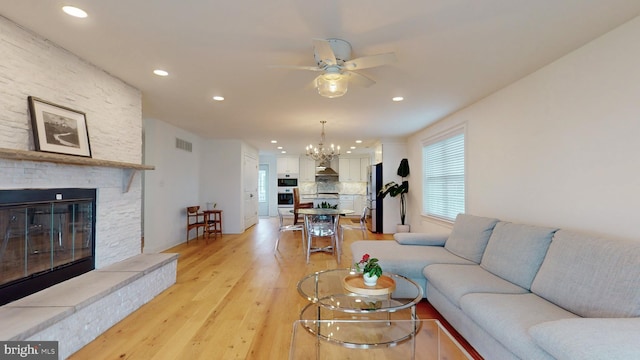 living room featuring ceiling fan with notable chandelier, a fireplace, and light hardwood / wood-style flooring