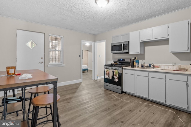 kitchen featuring a textured ceiling, stainless steel appliances, light hardwood / wood-style floors, white cabinetry, and sink