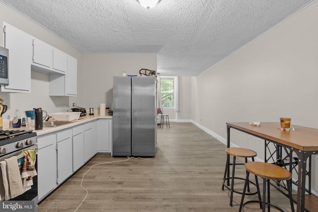 kitchen featuring stainless steel appliances, light wood-type flooring, a textured ceiling, white cabinetry, and sink