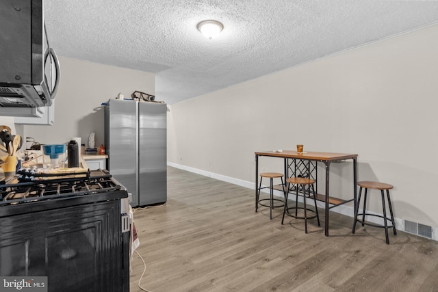 kitchen with stainless steel appliances, a textured ceiling, wood-type flooring, and a breakfast bar area