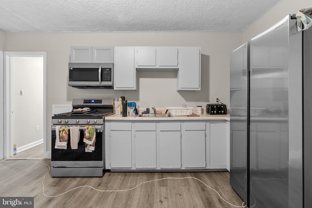 kitchen with sink, a textured ceiling, light hardwood / wood-style flooring, and appliances with stainless steel finishes