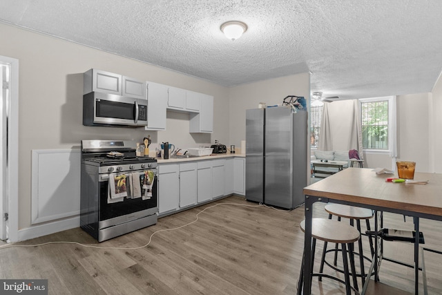 kitchen featuring stainless steel appliances, white cabinets, a textured ceiling, and light hardwood / wood-style flooring