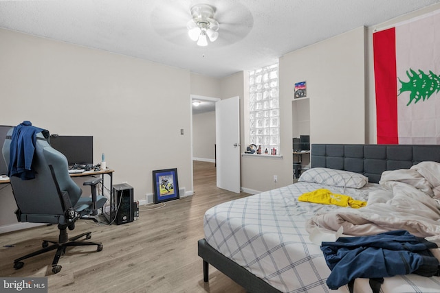 bedroom with a textured ceiling, ceiling fan, and light hardwood / wood-style flooring