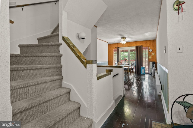 staircase with wooden walls, a textured ceiling, ceiling fan, and hardwood / wood-style flooring