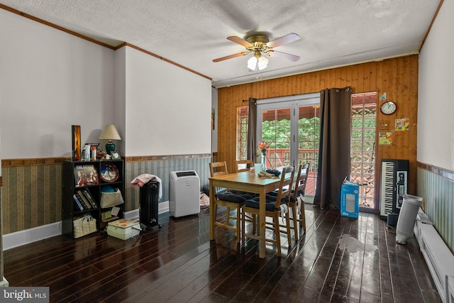 dining space with a textured ceiling, ceiling fan, ornamental molding, wood walls, and dark hardwood / wood-style floors