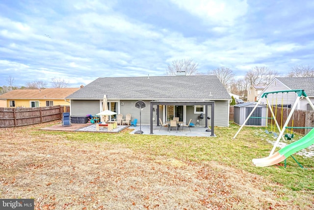 back of house featuring a lawn, a playground, a storage unit, and a patio