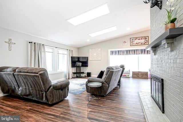 living room with a brick fireplace, vaulted ceiling with skylight, and dark hardwood / wood-style floors