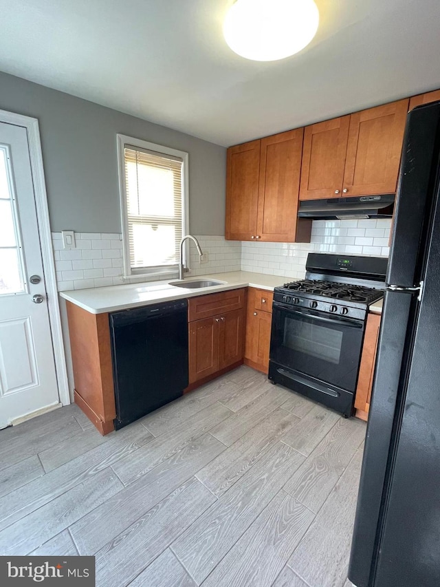 kitchen with sink, decorative backsplash, black appliances, and light wood-type flooring