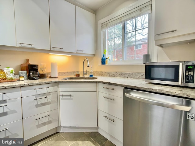 kitchen with sink, white cabinetry, light stone counters, light tile patterned floors, and appliances with stainless steel finishes