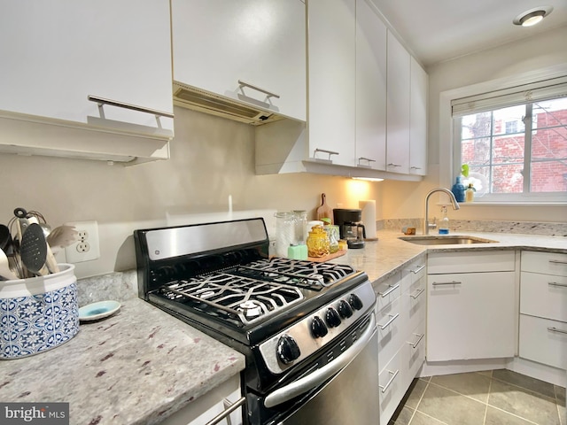 kitchen featuring light stone countertops, light tile patterned floors, white cabinets, stainless steel range with gas stovetop, and sink