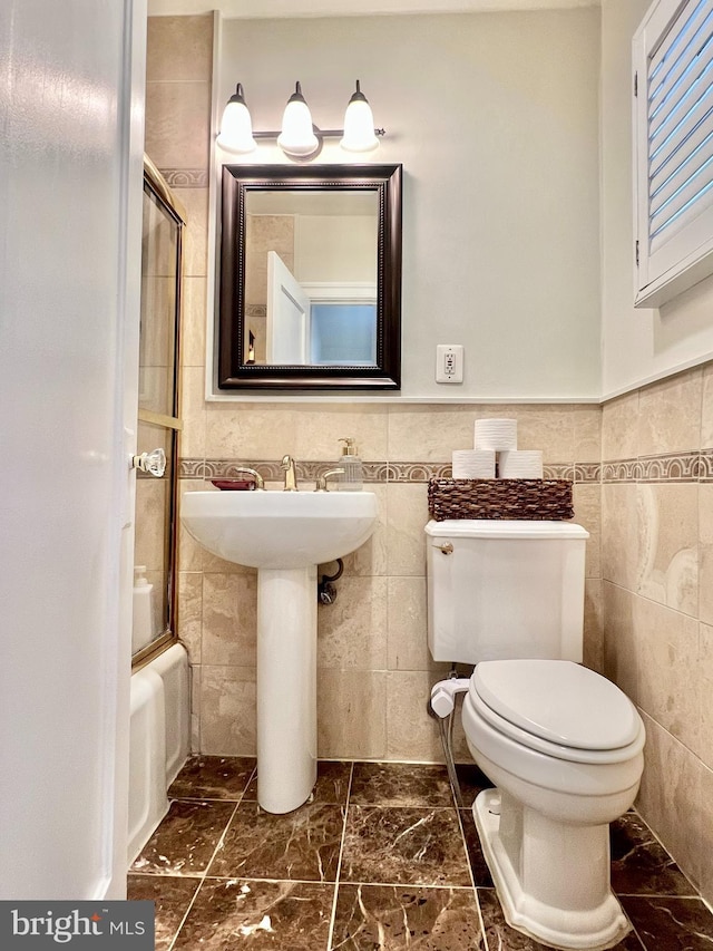 full bathroom with toilet, sink, tile walls, and shower / bath combination with glass door