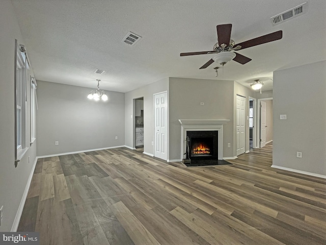 unfurnished living room featuring a textured ceiling, ceiling fan with notable chandelier, and hardwood / wood-style floors