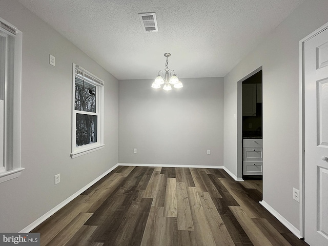 unfurnished dining area with dark wood-type flooring, a chandelier, and a textured ceiling