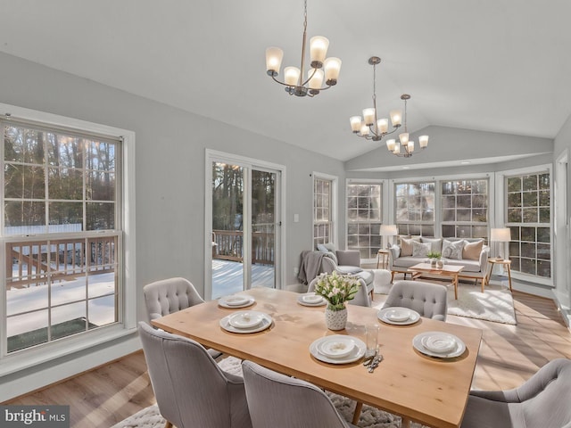 dining space with light hardwood / wood-style floors, vaulted ceiling, and an inviting chandelier