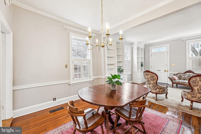 dining area featuring dark hardwood / wood-style flooring, crown molding, built in shelves, and a chandelier