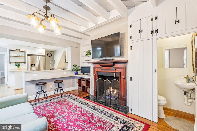 living room featuring a chandelier, beam ceiling, light hardwood / wood-style floors, and sink