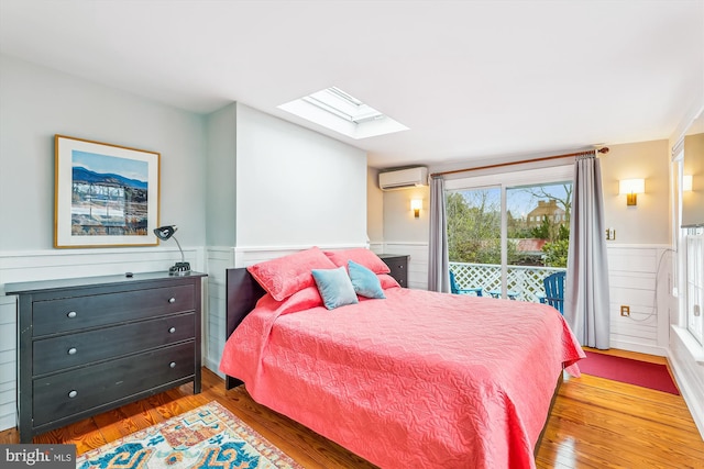 bedroom featuring a wall mounted air conditioner, access to exterior, a skylight, and wood-type flooring