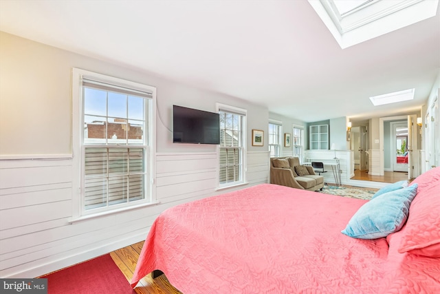 bedroom with multiple windows, wood-type flooring, and a skylight