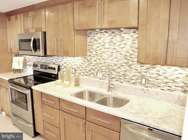 kitchen with light stone counters, appliances with stainless steel finishes, sink, and decorative backsplash