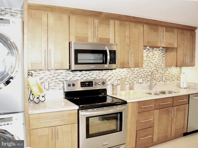 kitchen featuring appliances with stainless steel finishes, stacked washer / dryer, sink, decorative backsplash, and light stone counters