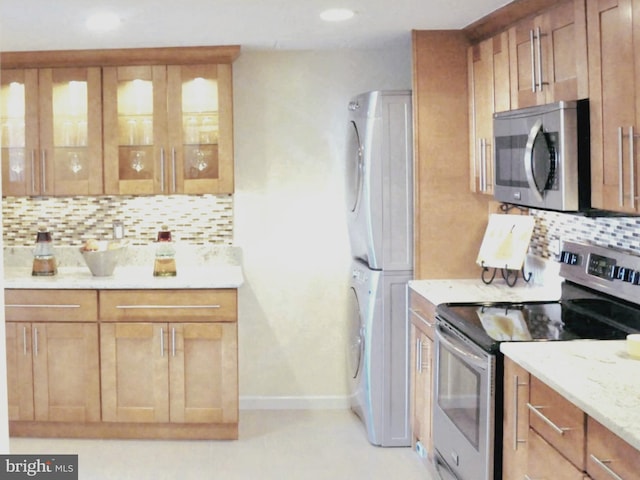 kitchen featuring tasteful backsplash, stainless steel appliances, light stone counters, and stacked washer / drying machine