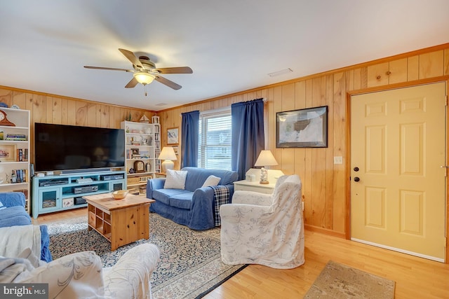 living room with ornamental molding, ceiling fan, light hardwood / wood-style floors, and wood walls