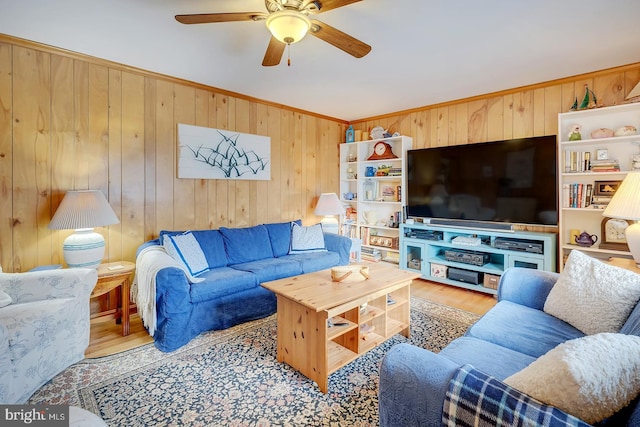 living room with ceiling fan, ornamental molding, wood walls, and light wood-type flooring