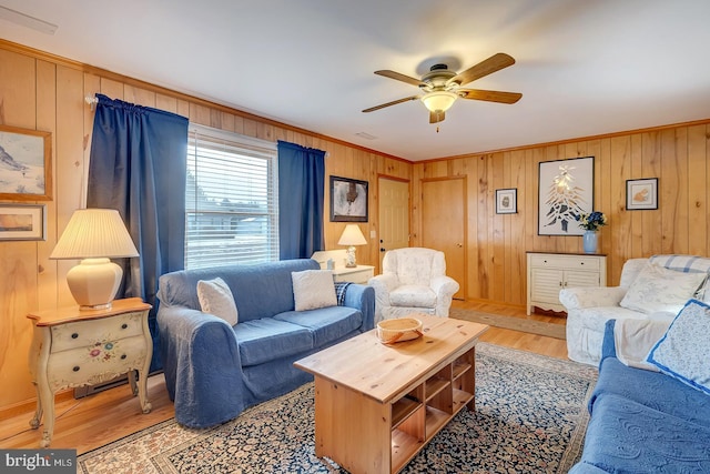 living room with ornamental molding, wooden walls, ceiling fan, and light hardwood / wood-style flooring