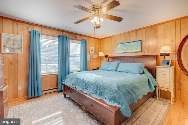 bedroom with crown molding, ceiling fan, baseboard heating, wooden walls, and light wood-type flooring